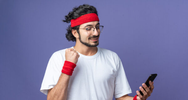 Smiling young sporty man wearing headband with wristband holding and looki