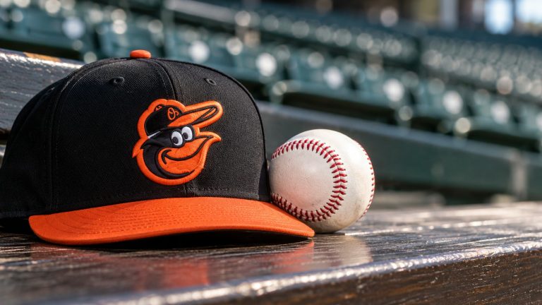 A black-and-orange Baltimore Orioles cap beside a baseball on a wooden bench.