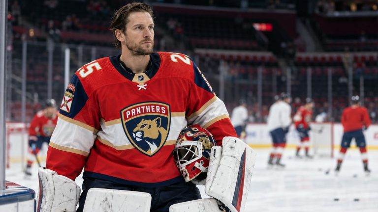 Jacob Markstrom in a red Florida Panthers No. 25 jersey holding a goalie mask beside the rink.