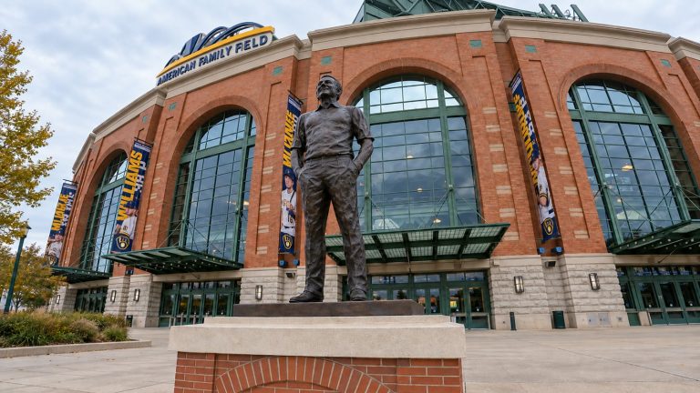 Bronze statue of Bob Uecker outside American Family Field, with the Brewers’ brick-and-glass ballpark entrance behind it.