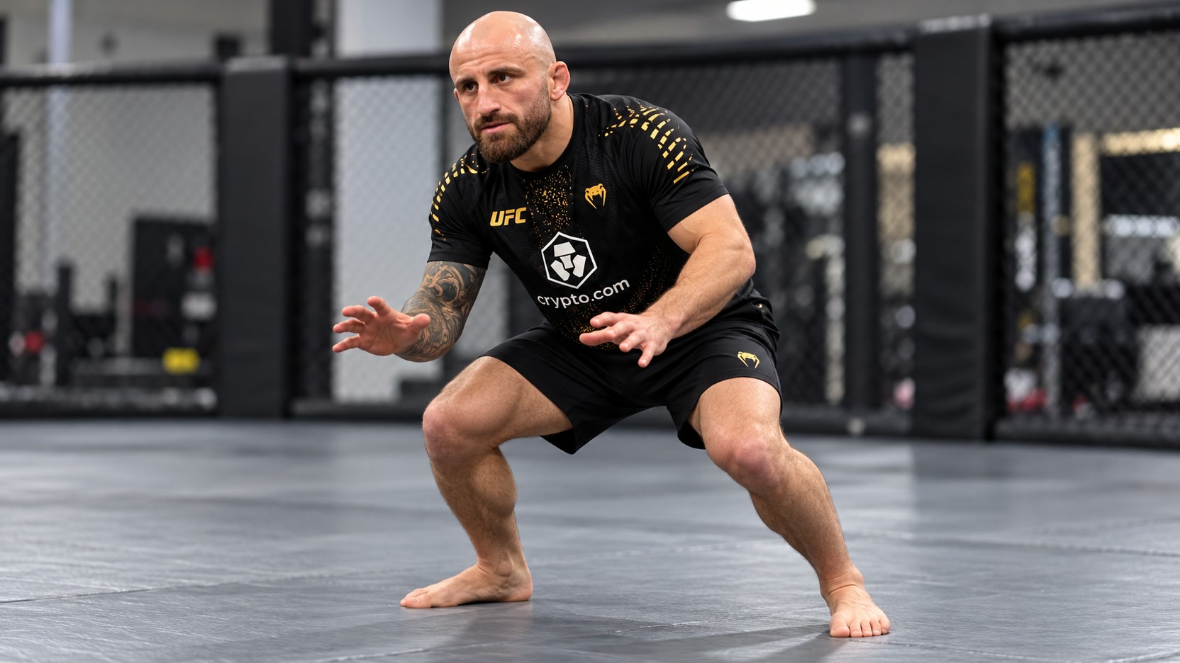 Alexander Volkanovski preparing in a wrestling stance Alexander Volkanovski in black-and-gold UFC training clothing holding a wrestling stance on gym mats beside an MMA cage.