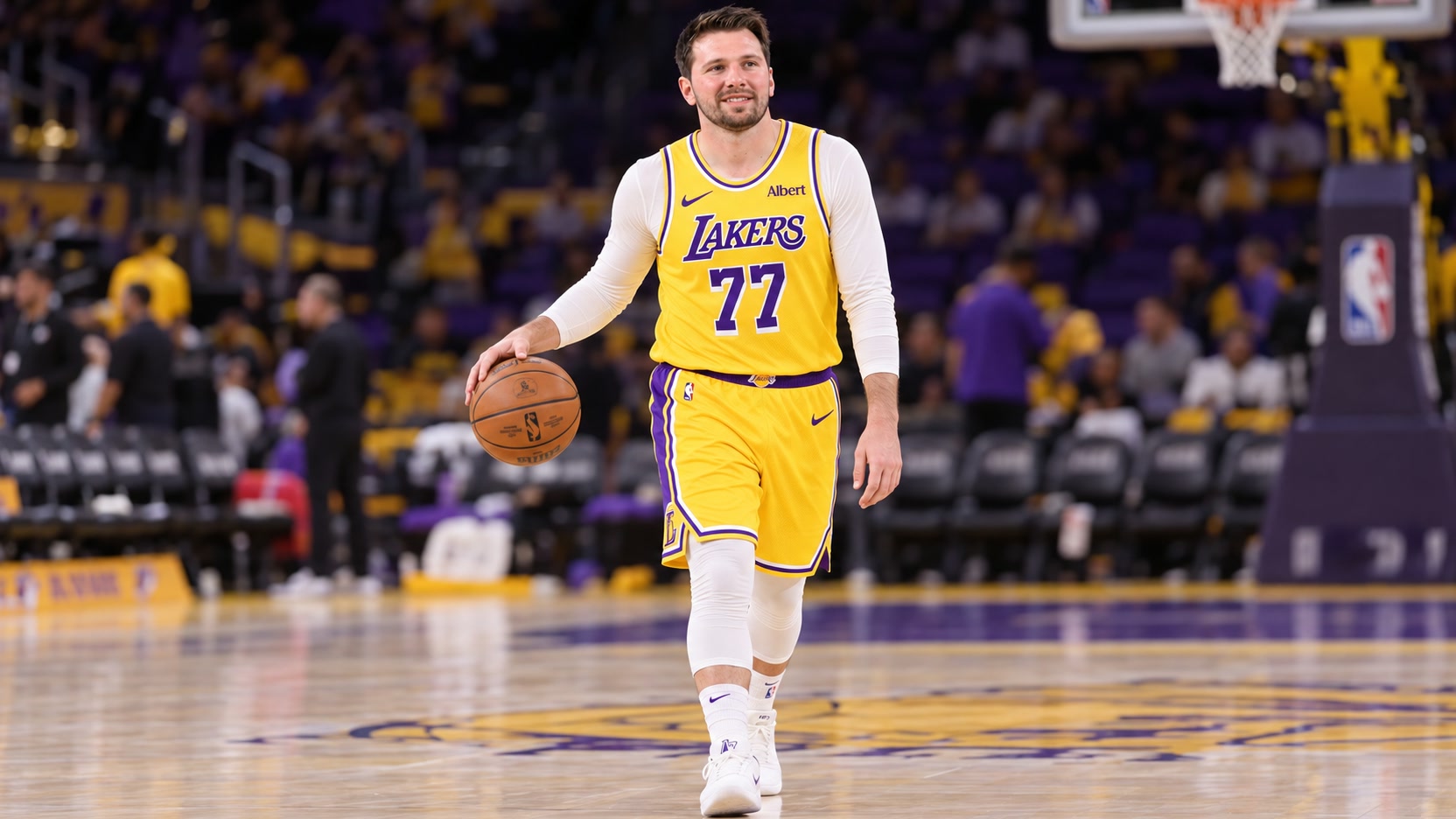 Luka Dončić in a gold Lakers No. 77 uniform and white warmup layers handling a basketball on an indoor court.