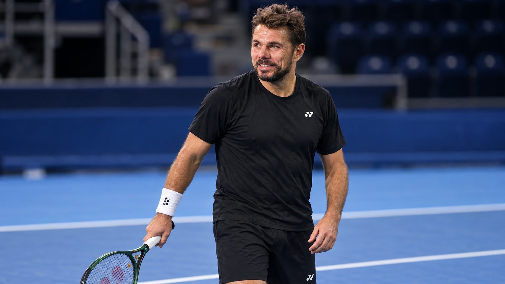 Stan Wawrinka in black Yonex training clothes holding a racket on an indoor hard court
