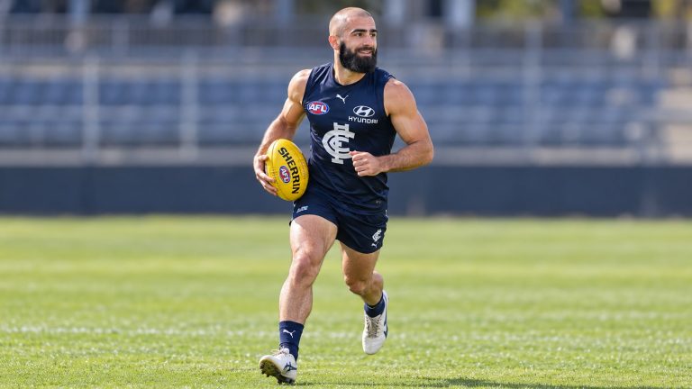 Adam Saad running with a yellow football in Carlton’s navy blue uniform.