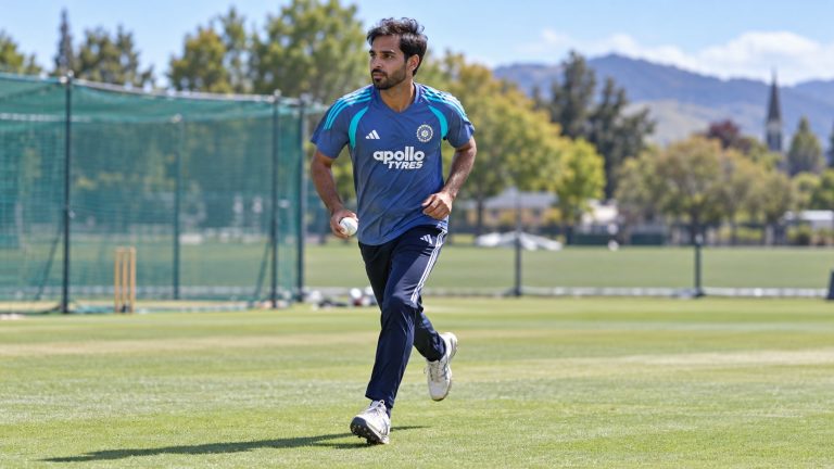 Bhuvneshwar Kumar holding a white cricket ball during a run-up in India’s blue and teal training kit.