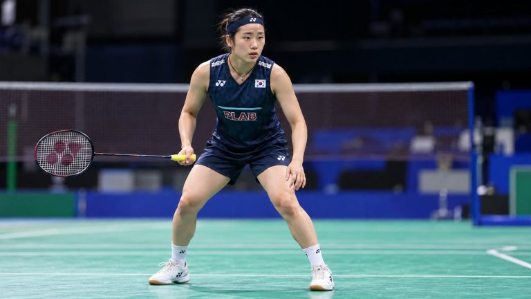 An Se-young holding a badminton racket in a ready stance, wearing a navy South Korea uniform and headband.