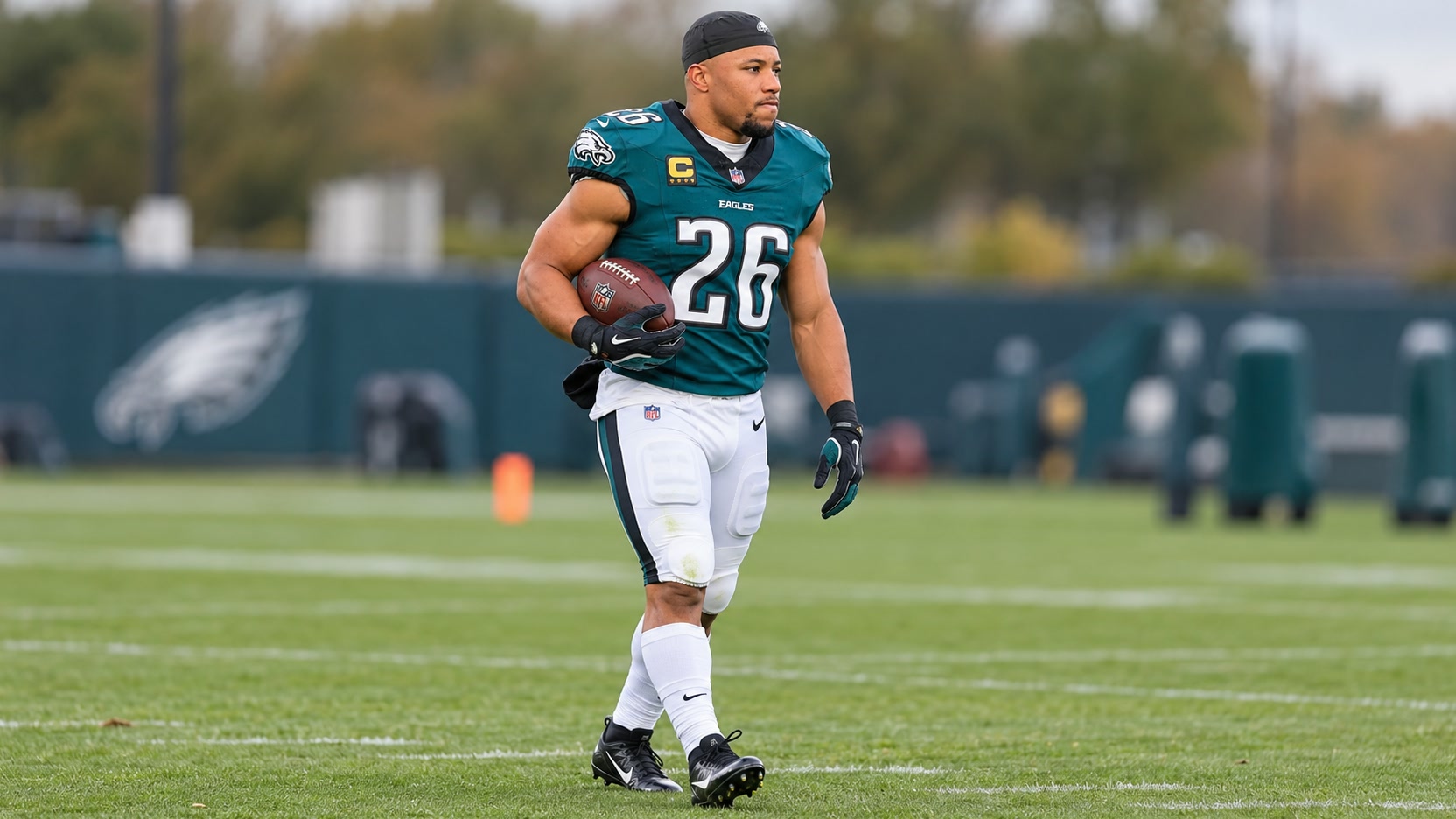 Saquon Barkley carrying a football in the Eagles’ midnight green number 26 jersey and white pants.