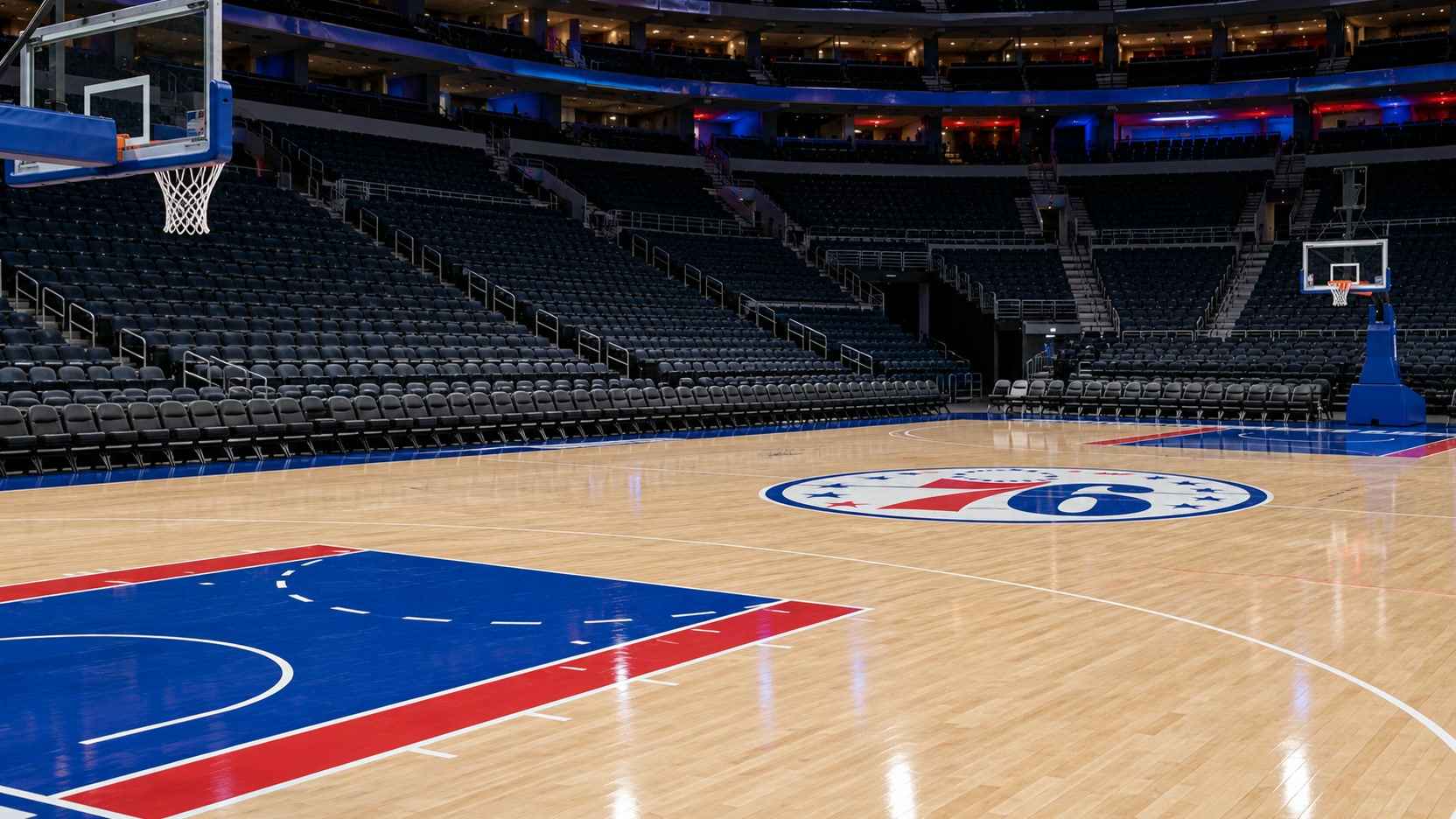 Philadelphia basketball home opener An empty basketball arena with a Philadelphia 76ers themed court, blue painted lanes and two baskets.