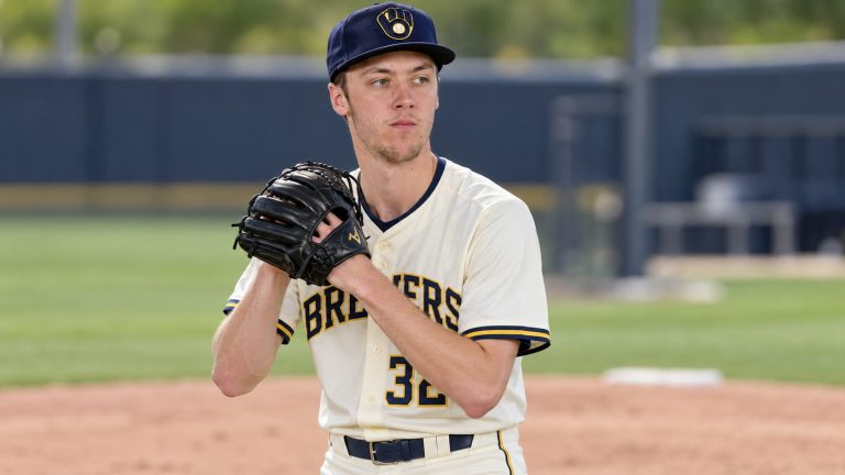 Jacob Misiorowski wearing a cream Brewers No. 32 uniform and navy cap, holding a black baseball glove during preparation.