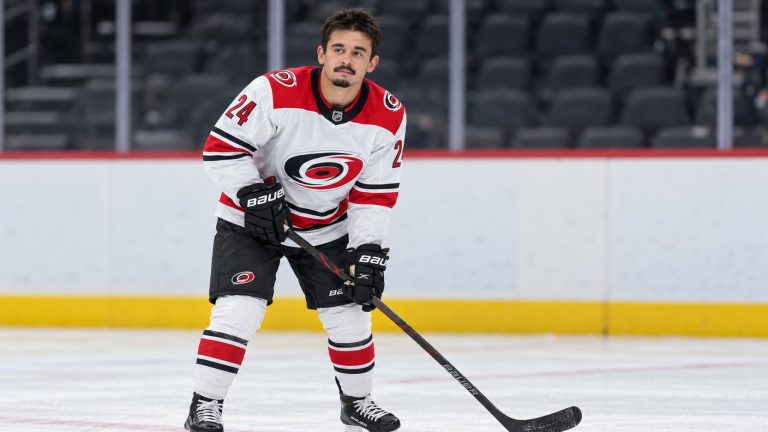 Seth Jarvis wearing a white Carolina Hurricanes No. 24 uniform and black gloves, holding a hockey stick on the ice.