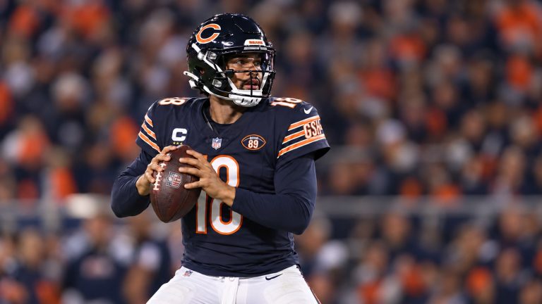 Caleb Williams in a navy Chicago Bears No. 18 jersey and helmet holds a football while looking downfield.