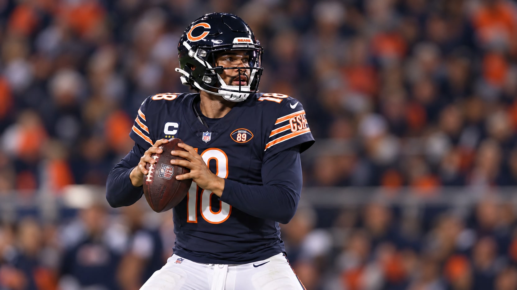 Caleb Williams in Chicago Bears uniform Caleb Williams in a navy Chicago Bears No. 18 jersey and helmet holds a football while looking downfield.