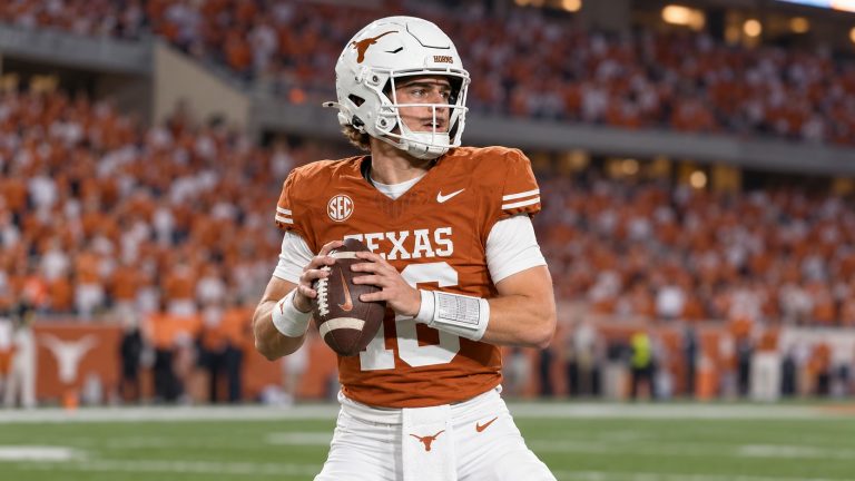 Arch Manning in a burnt orange Texas No. 16 jersey and white helmet holds a football while looking downfield.