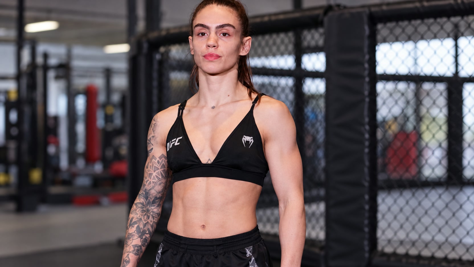 Nicolle Caliari Nicolle Caliari wearing a black UFC Venum training top beside an MMA cage.