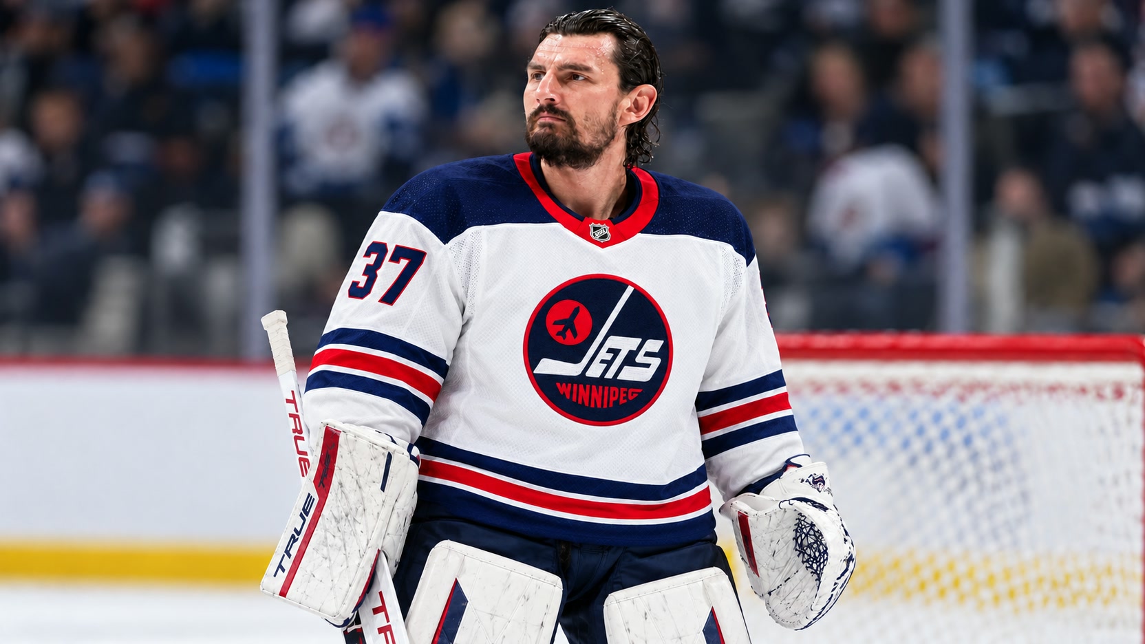 Connor Hellebuyck Connor Hellebuyck in a white Winnipeg Jets number 37 jersey with goalie gloves resting beside his body.