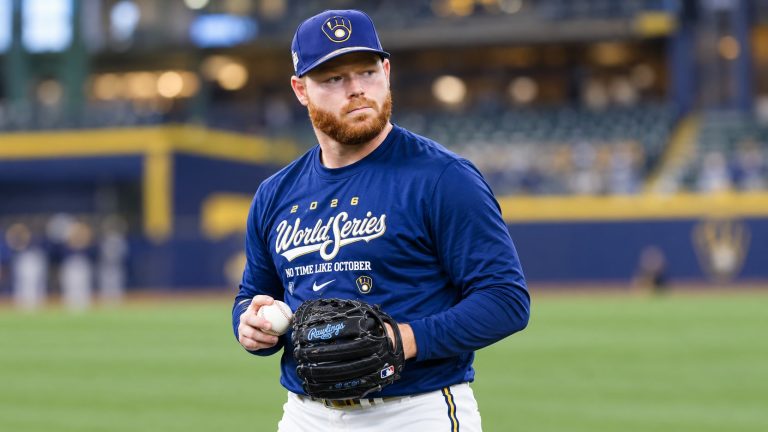 Brandon Woodruff in Brewers World Series workout clothing holding a baseball and black glove.