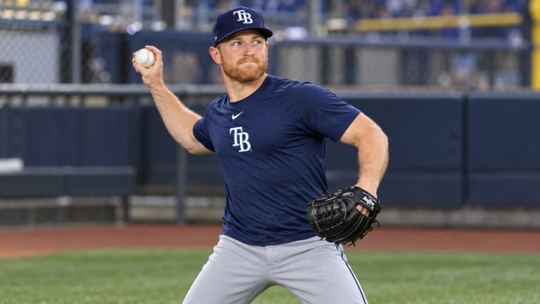 Drew Rasmussen warming up in a navy Rays shirt and cap, with a baseball in his right hand and glove on his left.