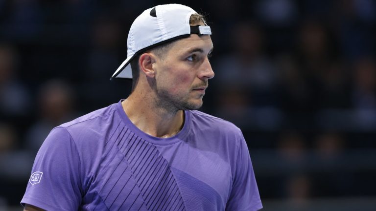 Jan-Lennard Struff in a purple tennis shirt and backwards white cap in an indoor arena.