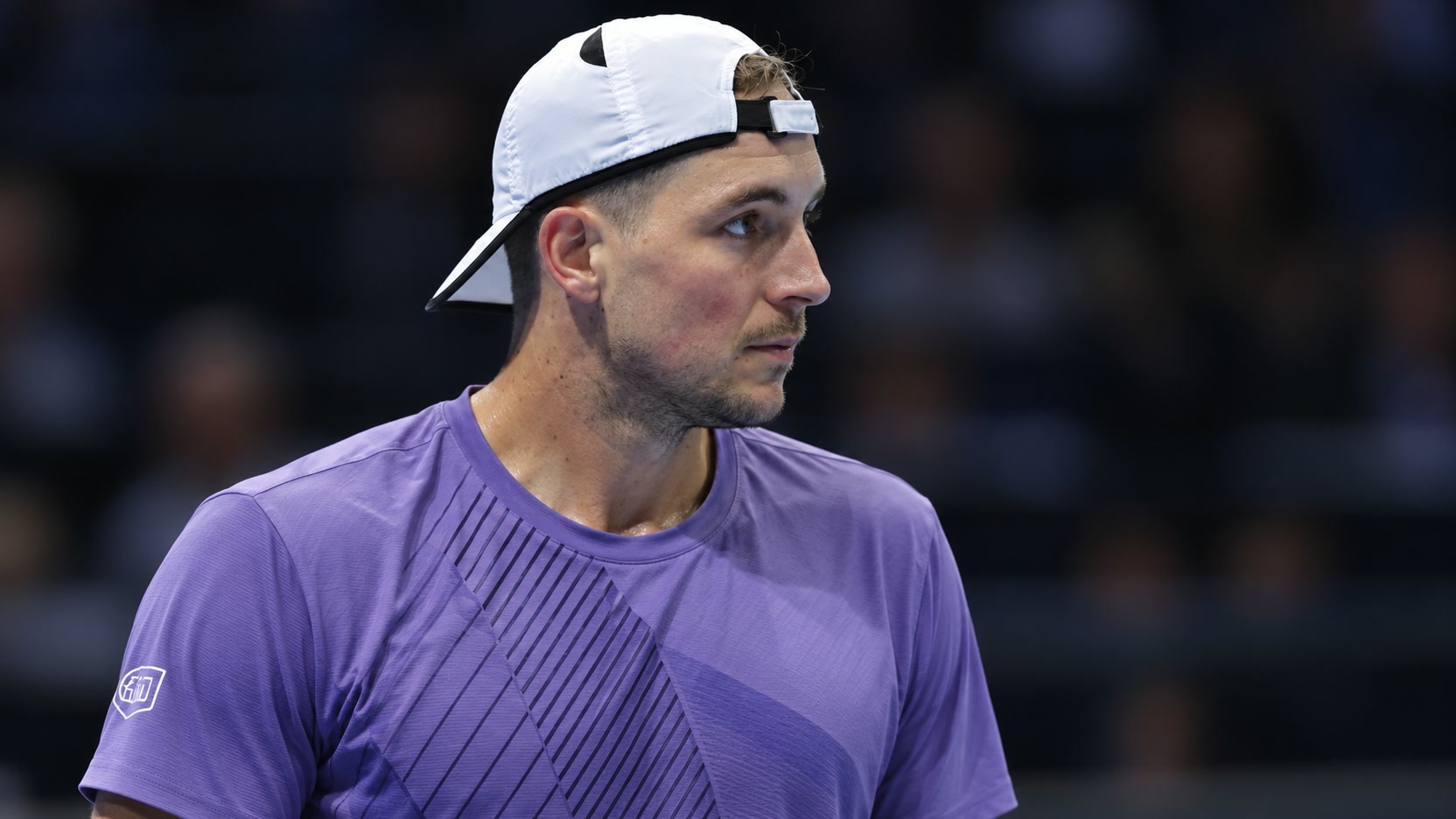 Jan-Lennard Struff in a purple tennis shirt and backwards white cap in an indoor arena.