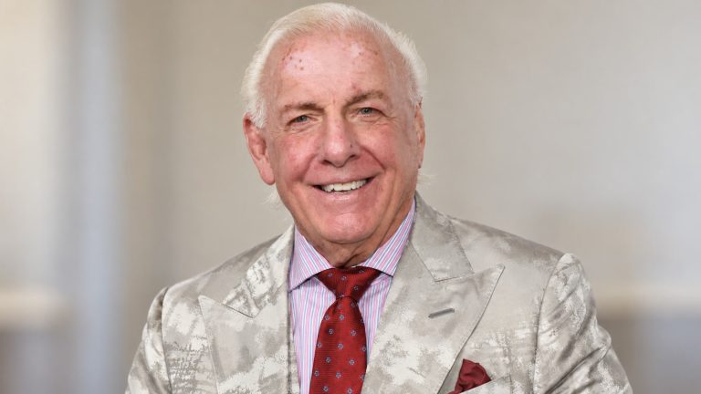 Ric Flair wearing a light silver patterned suit, striped shirt and burgundy tie.