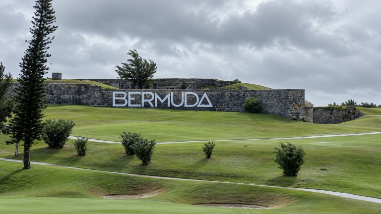 Rolling golf-course fairways beneath gray skies with trees and BERMUDA lettering on a stone wall.