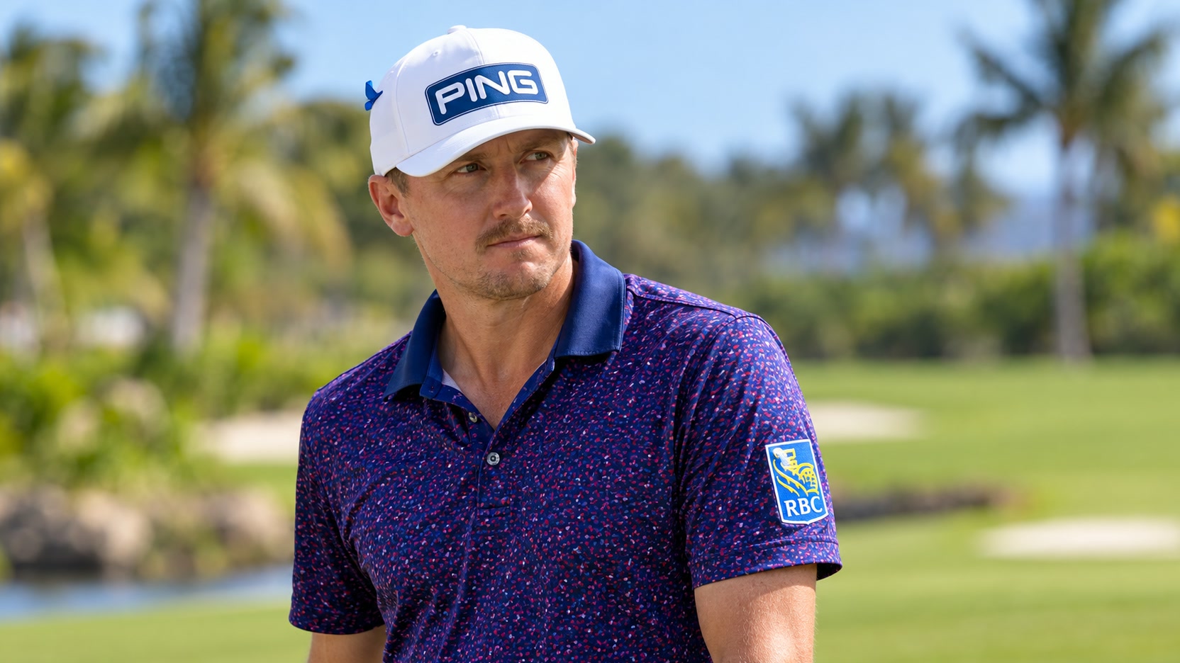 Mackenzie Hughes on a tropical golf course Mackenzie Hughes wearing a white PING cap and patterned navy golf polo with an RBC sleeve patch on a tropical golf course.
